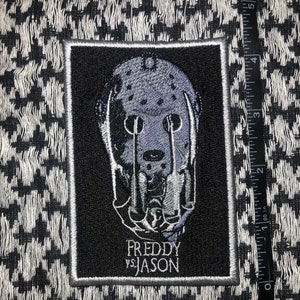 May include: Black and white embroidered patch featuring a white and gray Freddy Krueger mask with the text "FREDDY VS JASON" underneath.