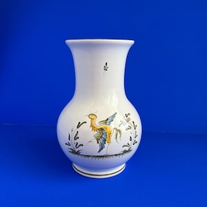 May include: White ceramic vase with a yellow and blue bird design. The vase has a round body and a narrow neck.