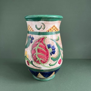 May include: A ceramic vase with a green rim and a cream base. The vase is decorated with a floral pattern in shades of red, blue, yellow, and green.