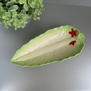 May include: A green ceramic serving dish shaped like a leaf with red flower accents. The dish has a raised centre section for serving.
