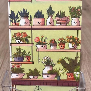 Könnte beinhalten: Eine Werbekarte mit verschiedenen Topfpflanzen auf Regalen, mit Preisen. Auf der Karte steht "Garten-Spar Challenge". Die Karte wird in einem transparenten Kunststoff-Displayständer präsentiert. Maße in cm.