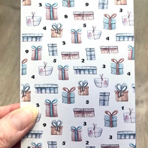 May include: A white card with a pattern of blue and brown gift boxes with numbers on them. The text "Geschenke-Spar-Challenge" and "Summe: 100" is printed on the card.