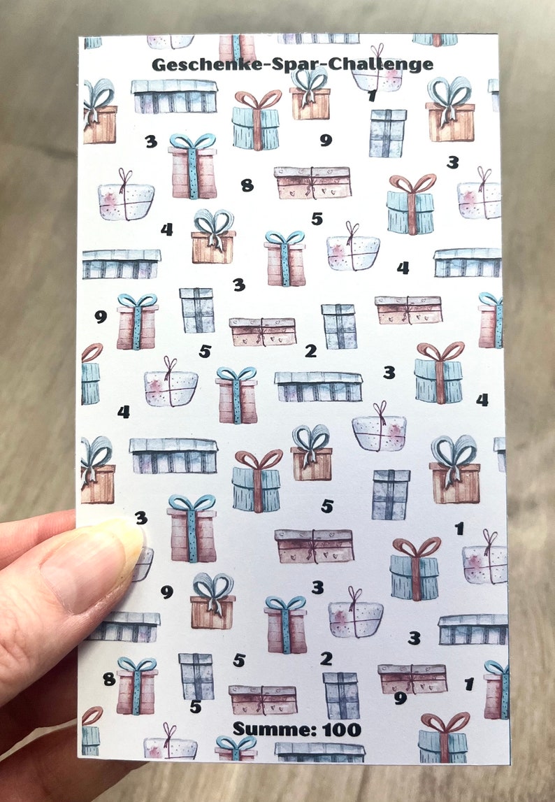 May include: A white card with a pattern of blue and brown gift boxes with numbers on them. The text "Geschenke-Spar-Challenge" and "Summe: 100" is printed on the card.