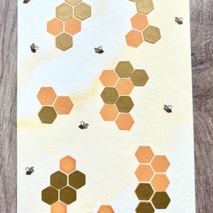 Könnte beinhalten: Eine beige Karte mit dem Text "BIENEN-SPAR-CHALLENGE" und "SPARSUMME: 150 €". Die Karte zeigt sechs Wabenformen in verschiedenen Größen und Farben, mit einer Bienenillustration in jeder Ecke.