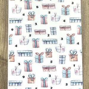 May include: A white sheet of paper with a pattern of brown, blue, and pink gift boxes. Each box has a number on it. The text "Geschenke-Spar-Challenge" and "Summe: 100" is at the top and bottom of the sheet.