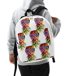 May include: A white backpack with a colorful pineapple pattern. The pineapple has sunglasses and a rainbow design.