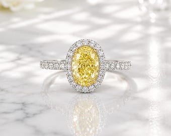 May include: A ring featuring a large oval-cut yellow center stone surrounded by a halo of small round white diamonds. The band is crafted from a silver-toned metal and is also set with a row of small round white diamonds along the shank.