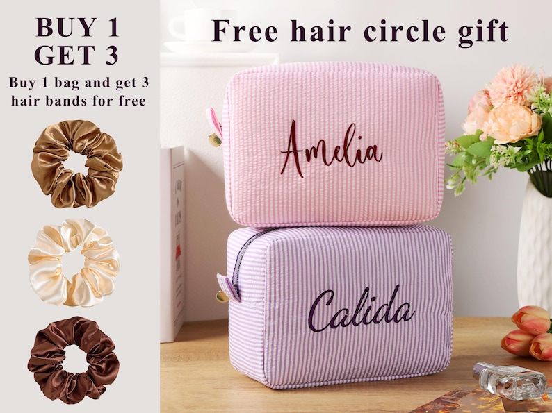 K&ouml;nnte beinhalten: Zwei quadratische Kosmetiktaschen, eine rosa und eine lavendelfarbene, &uuml;bereinander gestapelt. Auf der rosa Tasche ist der Name "Amelia" gestickt, auf der lavendelfarbenen Tasche steht "Calida". Drei Haargummis in Braun- und Cremet&ouml;nen sind ebenfalls zu sehen. Der Text "KAUFE 1 ERHALTE 3" steht oben.