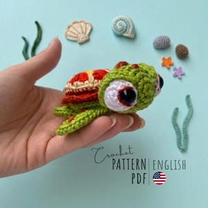 Può includere: Una tartaruga all'uncinetto con testa e arti verdi, guscio rosso e beige e grandi occhi neri. L'immagine include piccole creature marine all'uncinetto e il testo "Crochet PATTERN ENGLISH PDF".