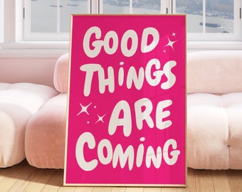 May include: A pink poster with the text "GOOD THINGS ARE COMING" in white, bubbly letters. The poster is framed in gold and is hanging on a wall.