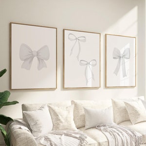 Puede incluir: Tres impresiones enmarcadas con diseños de lazos de acuarela blanca sobre un fondo blanco. Los marcos son de color madera clara.