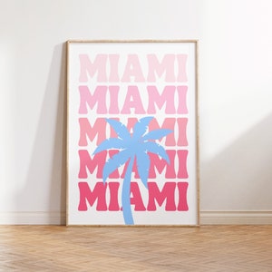 May include: A framed print with the word "Miami" repeated five times in a gradient of pink and red colors. A blue silhouette of a palm tree is centered in the middle of the print.