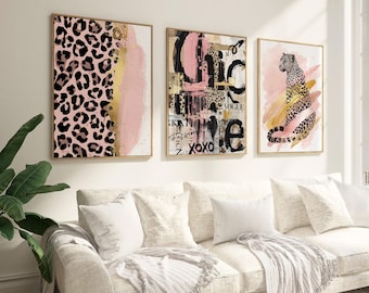 May include: Three framed wall art pieces with gold frames. The art features a leopard print, abstract designs with pink and black accents, and a leopard illustration. The artwork hangs above a cream-colored sofa.