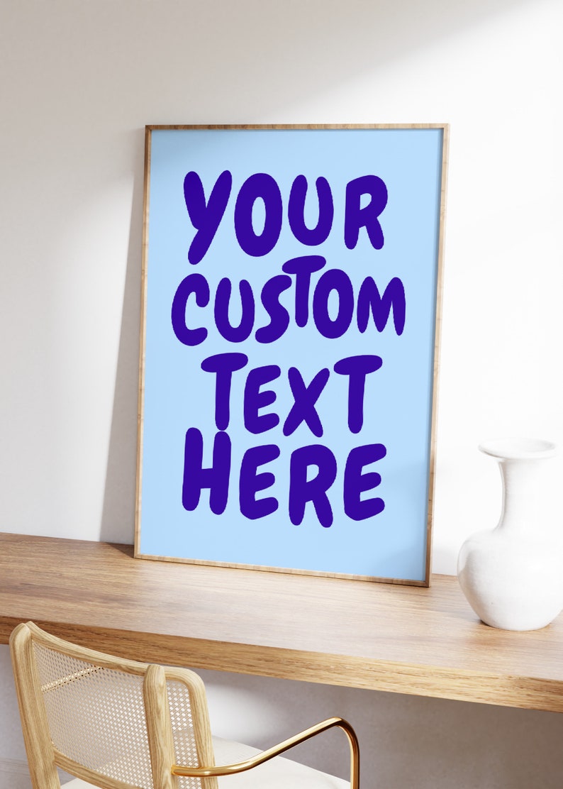 May include: A framed poster with a light blue background and the text "YOUR CUSTOM TEXT HERE" in bold, purple letters. The poster is sitting on a wooden desk with a white vase.
