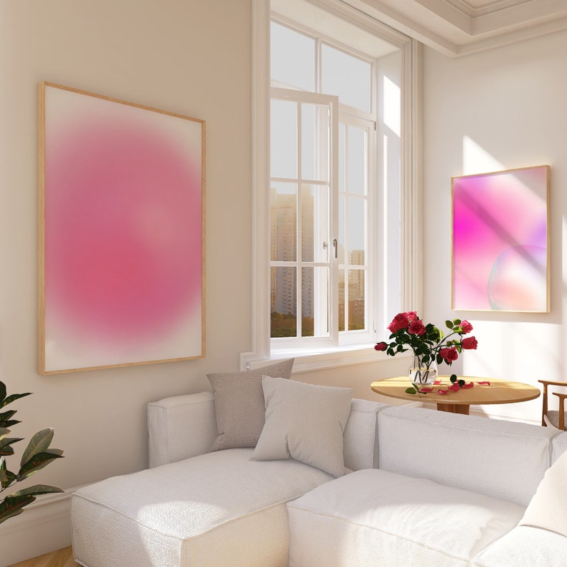 Puede incluir: Un sof&aacute; blanco con dos almohadas en una sala de estar con una ventana grande, una mesa de madera con un jarr&oacute;n de rosas rojas y dos pinturas abstractas en la pared. Una pintura es rosa y la otra es un degradado de rosa y morado.