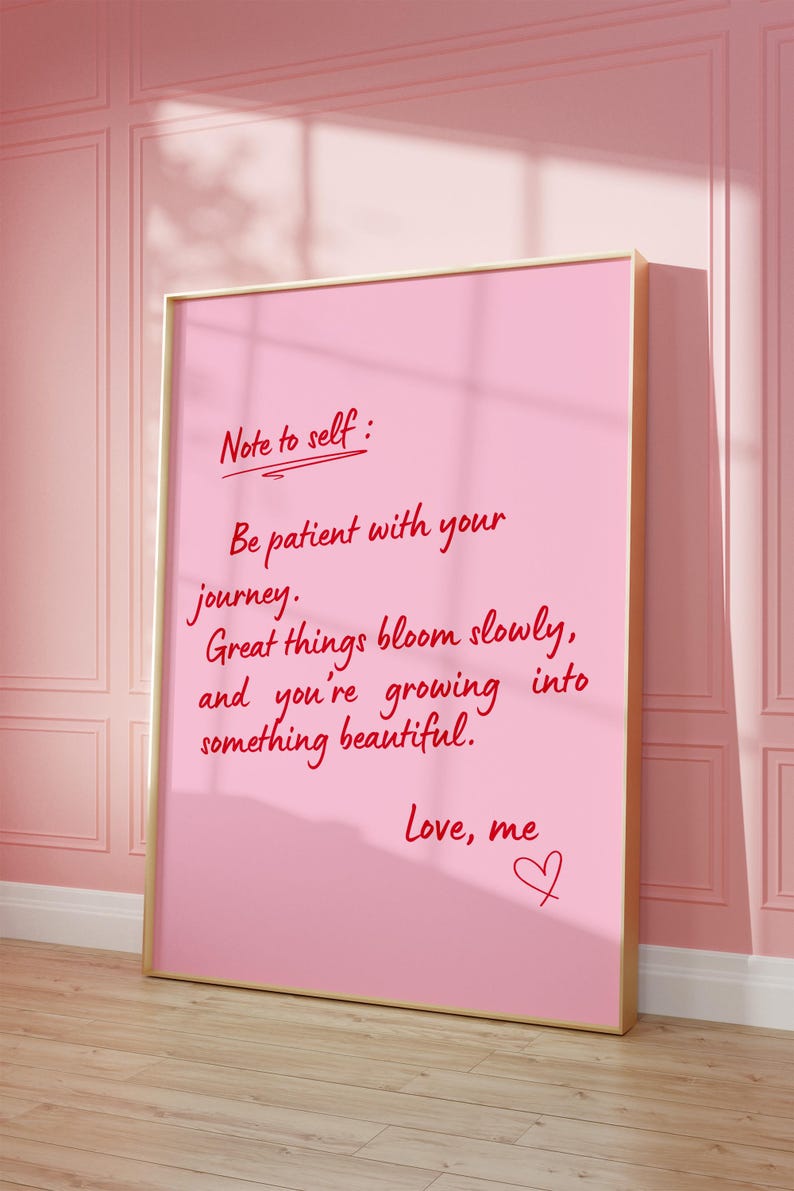 May include: A pink framed print with the text "Note to self: Be patient with your journey. Great things bloom slowly, and you're growing into something beautiful. Love, me" in red script. The print is leaning against a pink wall.