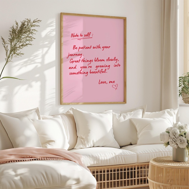 May include: A framed pink print with handwritten text that reads "Note to self: Be patient with your journey. Great things bloom slowly, and you're growing into something beautiful. Love, me." The frame is a light brown color.
