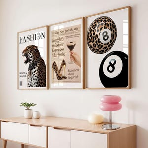 Puede incluir: Tres impresiones artísticas enmarcadas con marcos dorados. Las impresiones presentan un leopardo, un cóctel y una bola de billar. La primera impresión dice "FASHION" y "Wild Is a Neutral." La segunda impresión dice "Tonight's mission: Espresso Martinis!" La tercera impresión muestra una bola 8 con estampado de leopardo.