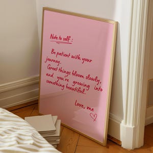 May include: A pink framed print with the text "Note to self: Be patient with your journey. Great things bloom slowly, and you're growing into something beautiful. Love, me." The frame is gold.