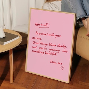 May include: A pink framed sign with the text "Note to self: Be patient with your journey. Great things bloom slowly, and you're growing into something beautiful. Love, me" written in red script.