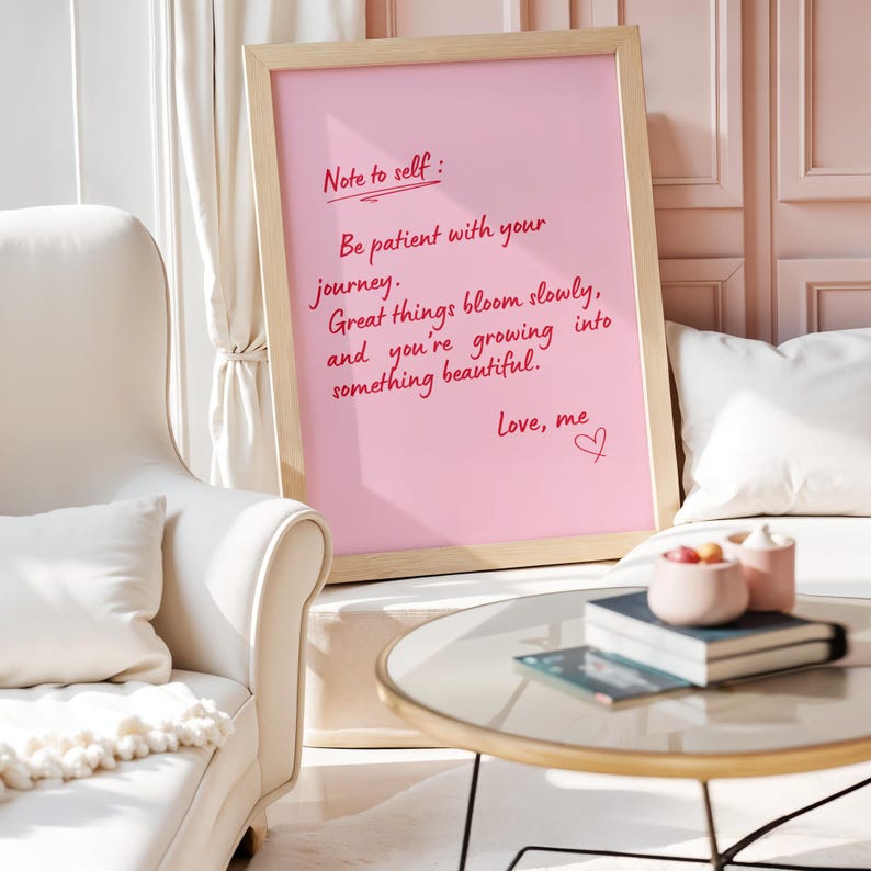 May include: A framed pink print with the handwritten text "Note to self: Be patient with your journey. Great things bloom slowly, and you're growing into something beautiful. Love, me." The frame is light wood.