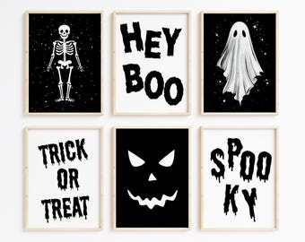 May include: Six framed Halloween-themed art prints. The prints feature a skeleton, a ghost, a jack-o'-lantern face, and the phrases "Hey Boo", "Trick or Treat", and "Spooky" in black and white against a black background.