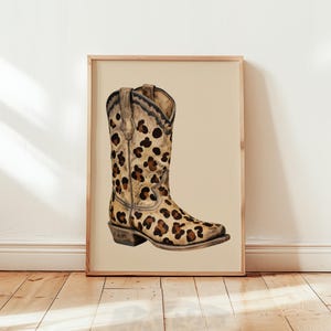 May include: A framed print showing a watercolour illustration of a cowboy boot. The boot features a leopard print pattern in brown and tan hues. The artwork is set against a neutral background.