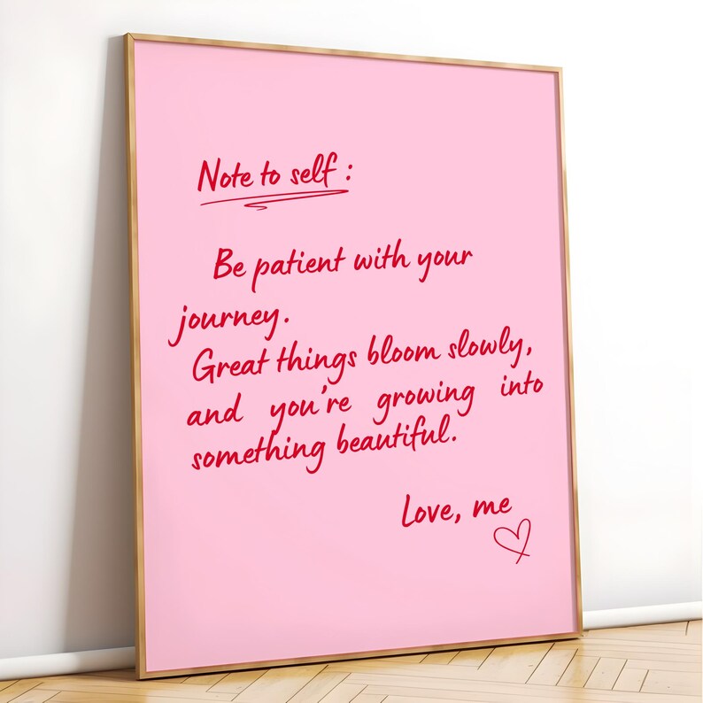 May include: A framed pink print with handwritten red text. The text reads "Note to self: Be patient with your journey. Great things bloom slowly, and you're growing into something beautiful. Love, me."