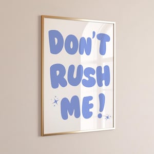 May include: A framed print with a white background and blue text that reads "Don't Rush Me!" with two small stars on either side of the text.