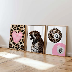 May include: Three framed art prints. The first features a pink heart on a leopard print background. The second depicts a roaring leopard with jewelry. The third shows a leopard print 8-ball and a pink 8-ball.