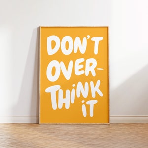 Op de afbeelding: Een gele geframed poster met witte tekst die "DON'T OVER-THINK IT" zegt.