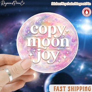 Puede incluir: Una pegatina redonda con un diseño de galaxia colorido en tonos rosa, morado y azul. La pegatina presenta las palabras "copy, moon, joy" en blanco, con una tipografía estilizada. Es resistente al agua y se puede usar como llavero, imán o pin.