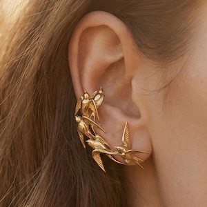 Puede incluir: Una taza de cerámica blanca con un asa negra y el texto "But First, Coffee" en negrita negra. La taza se encuentra sobre un fondo borroso, sugiriendo un ambiente acogedor.