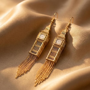 May include: A pair of gold-toned drop earrings shaped like the Elizabeth Tower, featuring a detailed clock face on each side and a dangling fringe of fine gold chains attached to the base of the tower structure, suspended from simple wire hooks.