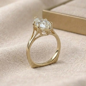 Op de afbeelding: Een gouden ring met een grote, peervormige diamant. De ring heeft een delicaat, open ontwerp rond de diamant en een gladde, gepolijste band. De ring staat tegen een neutrale achtergrond.