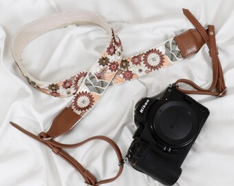 May include: An embroidered camera strap with a floral design in shades of brown, pink, and green. The strap has leather accents and is paired with a black Nikon camera. The text "ST-725" is visible.