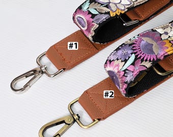 May include: Two brown leather camera straps with silver and gold clasps. The straps are decorated with colorful embroidered floral patterns. The straps are labeled #1 and #2.