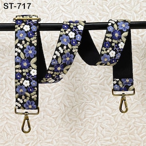 May include: A black floral embroidered bag strap with blue and white flowers and green leaves. The strap has gold-colored metal hardware and the text "ST-717" at the top.
