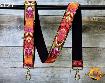 May include: An adjustable strap with a black and white floral pattern and gold metal clasps. The strap is made of woven fabric and features a colourful floral design. The strap is shown hanging from a wooden surface. The text "ST27" is visible in the top left corner of the image.