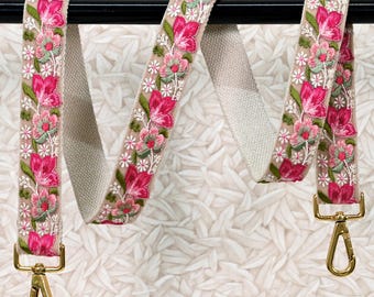 May include: A beige canvas strap with pink floral embroidery. The strap has gold metal clasps on each end. ST-660 is printed on the top left corner of the image.