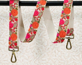May include: A white canvas strap with a floral embroidered design in pink, orange, and gold. The strap has two gold metal clasps. ST-661