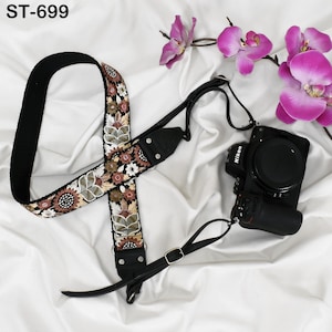 May include: An embroidered camera strap with a floral pattern in brown, cream, and green. The strap is connected to a black Nikon camera. The text "ST-699" is visible in the upper left corner.