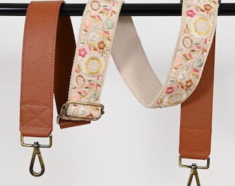 May include: Two adjustable straps for bags. One strap is brown leather with a gold clasp. The other strap is a beige canvas with a floral embroidery pattern and a gold buckle.