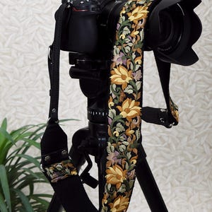 May include: A black Nikon camera with a floral embroidered strap featuring yellow, green, and purple flowers. The camera is mounted on a black tripod. The text "ST-786" is in the top left corner.