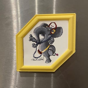 May include: A framed illustration of a gray elephant wearing headphones and a belt, with a yellow frame. The elephant is drawn in a cartoon style, with its trunk raised and one leg bent. The frame is a bright yellow color.