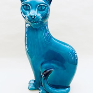 Könnte beinhalten: Glänzende, türkisfarbene Keramik-Katzenfigur. Die Katze sitzt mit eingerolltem Schwanz. Die Figur hat ein schlankes, modernes Design mit spitzen Ohren und detaillierten Gesichtszügen.