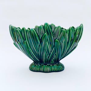 Könnte beinhalten: Eine grüne Keramikschale mit einem strukturierten, blattartigen Design. Die Schale hat einen gewellten Rand und einen Sockel. Die Farbe ist ein tiefes, glänzendes Grün mit weißen Akzenten. Die Schale ist wahrscheinlich für dekorative Zwecke.