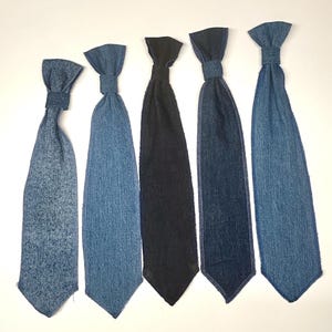 Op de afbeelding: Vijf denim stropdassen in verschillende tinten blauw en zwart zijn gerangschikt tegen een witte achtergrond. De stropdassen hebben een klassieke vorm met een knoop aan de bovenkant en een puntige onderkant. De stof lijkt een zacht denim materiaal te zijn.