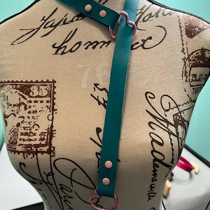 May include: Teal leather choker with pink heart-shaped metal accents and two silver metal rings.