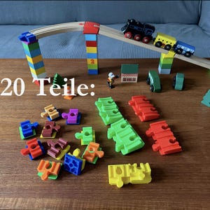 Könnte beinhalten: Ein hölzernes Spielzeug-Zugset mit Brücke, bunten Blöcken und Waggons. Das Set enthält eine schwarze Lokomotive, einen gelben Wagen und einen blauen Wagen. Der Text "20 Teile:" ist sichtbar.